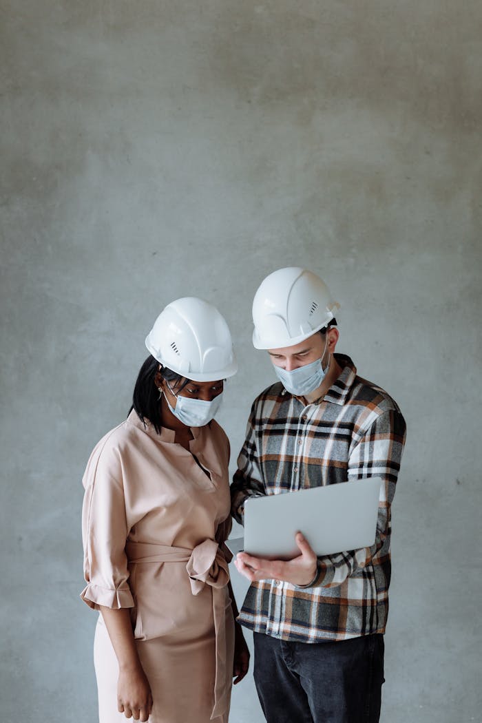 A Man and a Woman Wearing Face Mask while Looking at the Screen of a Laptop